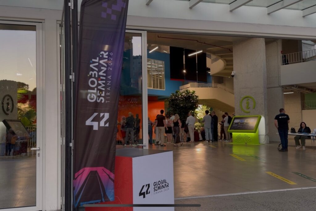 Acceso al 42 Global Seminar 2026 en Tirana, con la señalética del evento y varios asistentes en el interior.